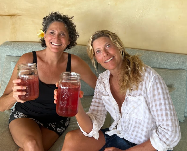 Two smiling women in their mid-50s, best friends since childhood, showcasing their health and wellness product. They hold large mason jars filled with a vibrant clean electrolyte, symbolizing their journey and dedication to wellness. The text reads 'EMBRACE THE PURITY, FEEL THE FREQUENCY, AND BE PART OF OUR STORY,' highlighting the brand's focus on natural, pure ingredients. The image captures the essence of friendship, entrepreneurship, and holistic health. It appeals to female entrepreneurship, and health